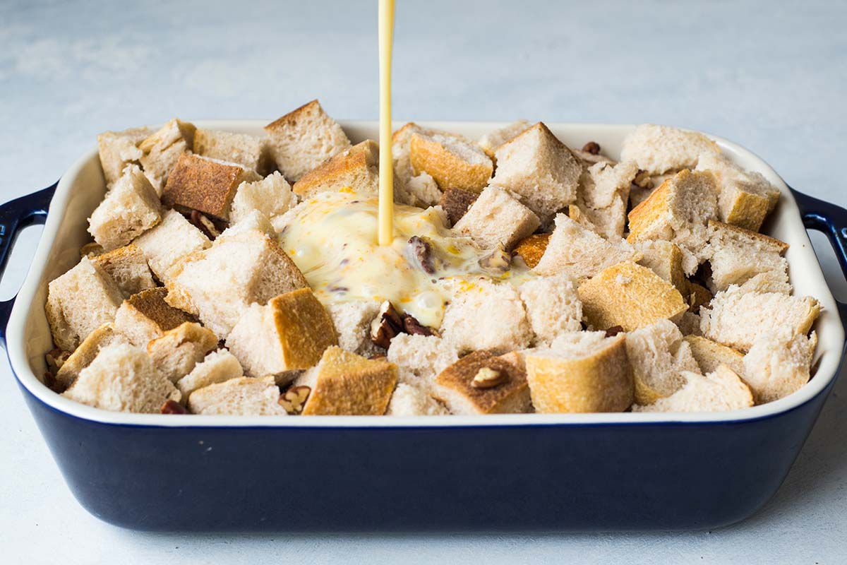 An egg mixture being poured on cubed bread in a casserole dish