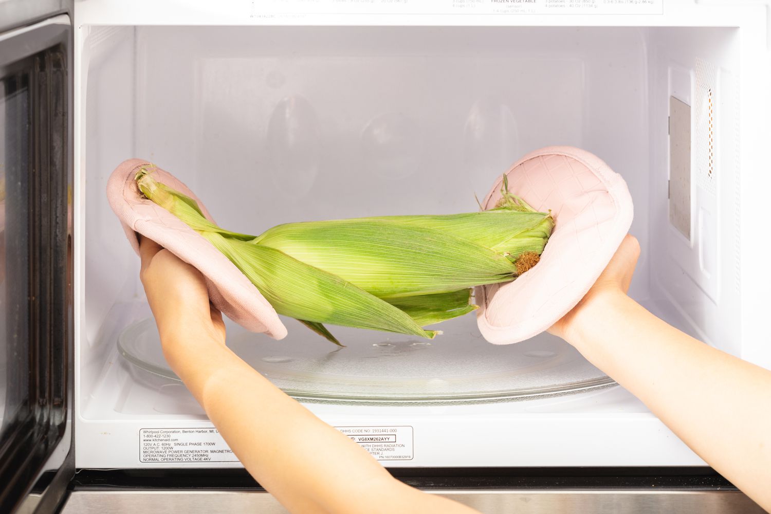 Using pot holders to remove a corn on the cob from a microwave.