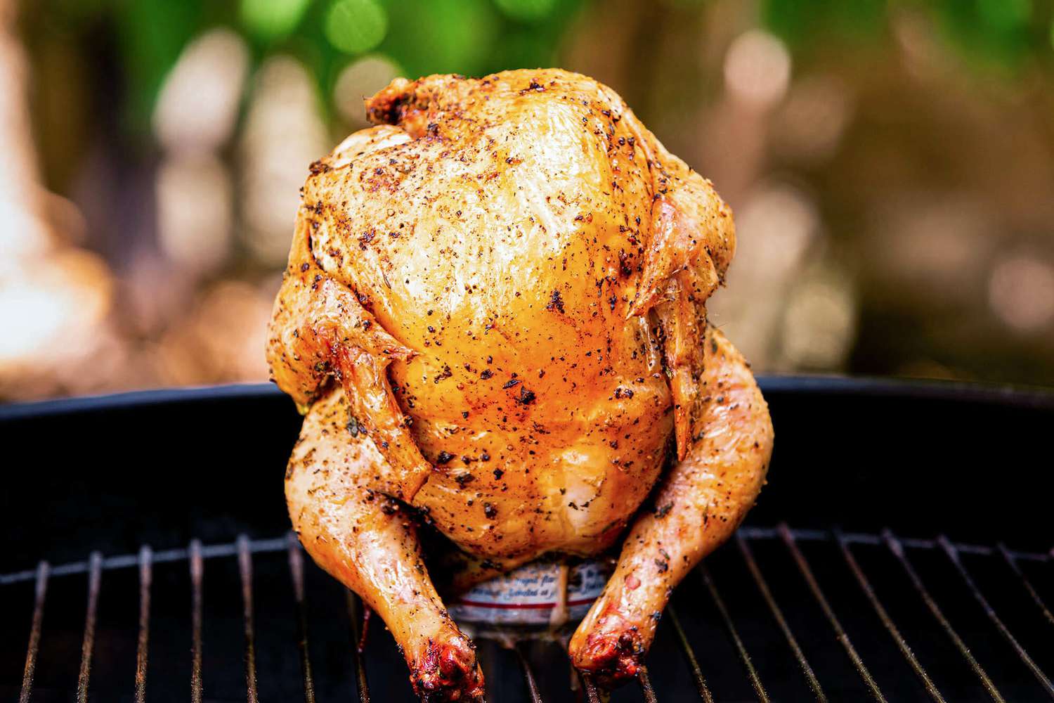 A whole chicken sits atop a beer can on a grill