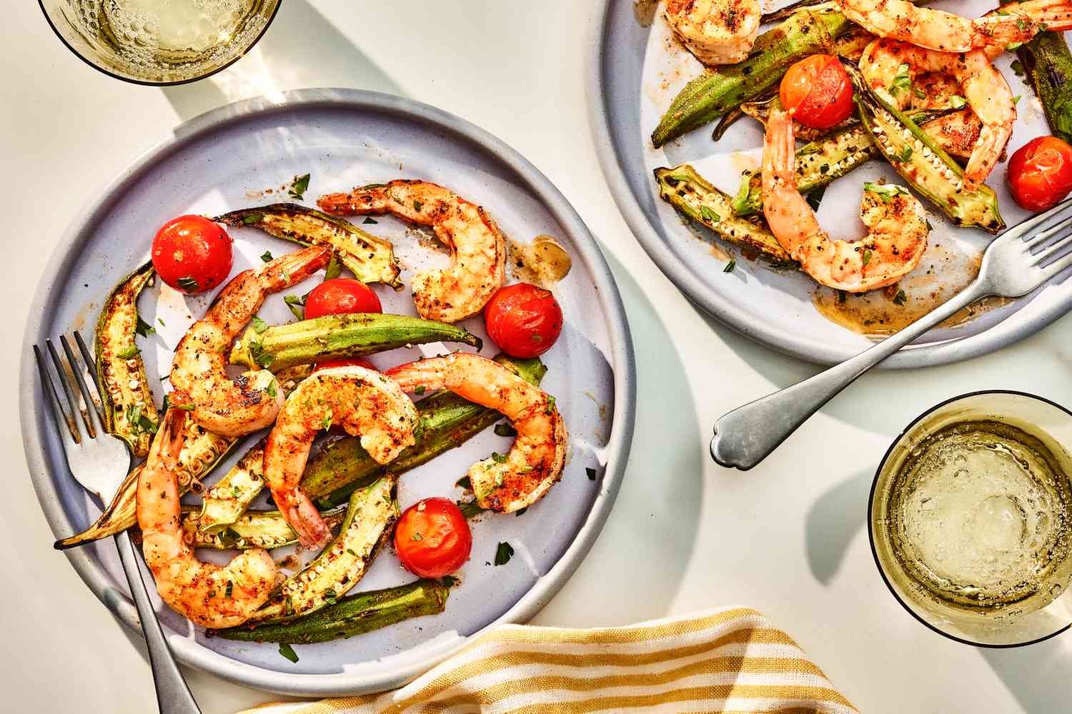 pan-roasted shrrimp and okra served on two plates at a table setting with glasses of water and a table napkin