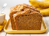Spiced Dulce de Leche Banana Bread (Some of It Sliced) on a Platter, and in the Surroundings, a Bowl With More Dulce de Leche and Bananas