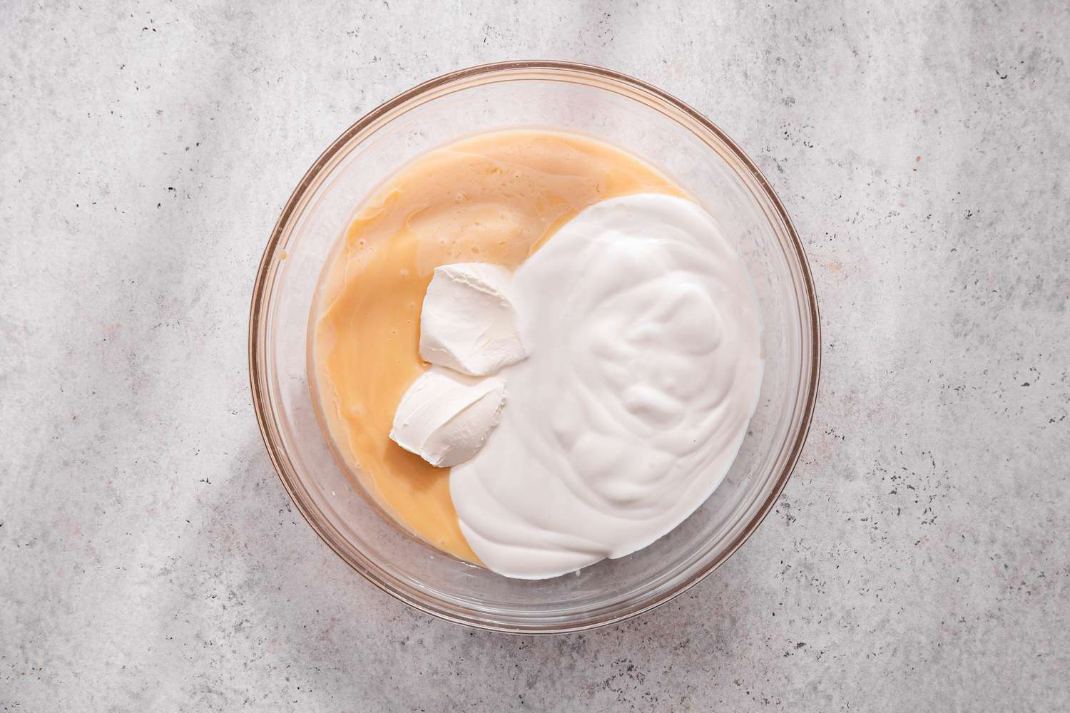 Sweetened condensed milk, heavy cream, and sour cream in a glass mixing bowl