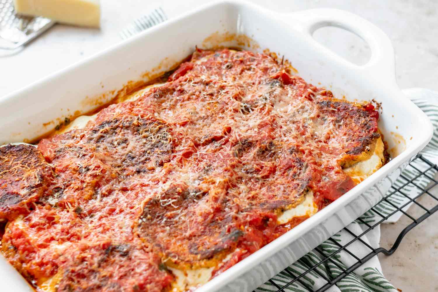 A finished, baked eggplant parmesan in a white casserole dish