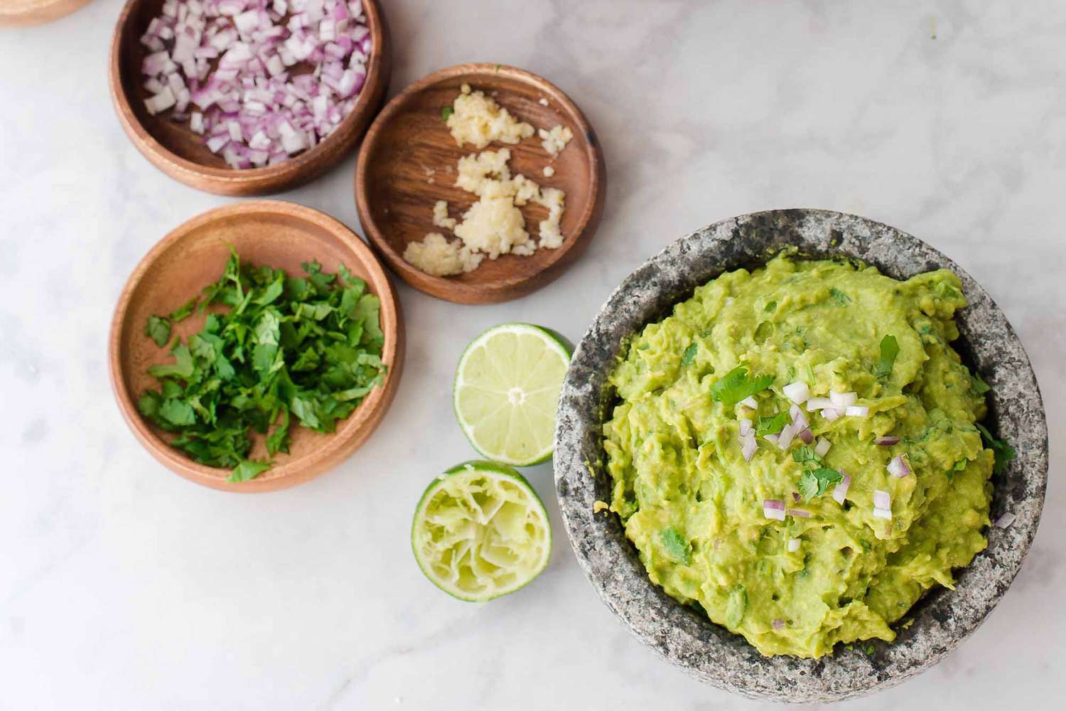 Guacamole with lime and cilantro - bowl of guacamole with smaller bowls of onion, cilantro, garlic and lime nearby and a big bowl of chips