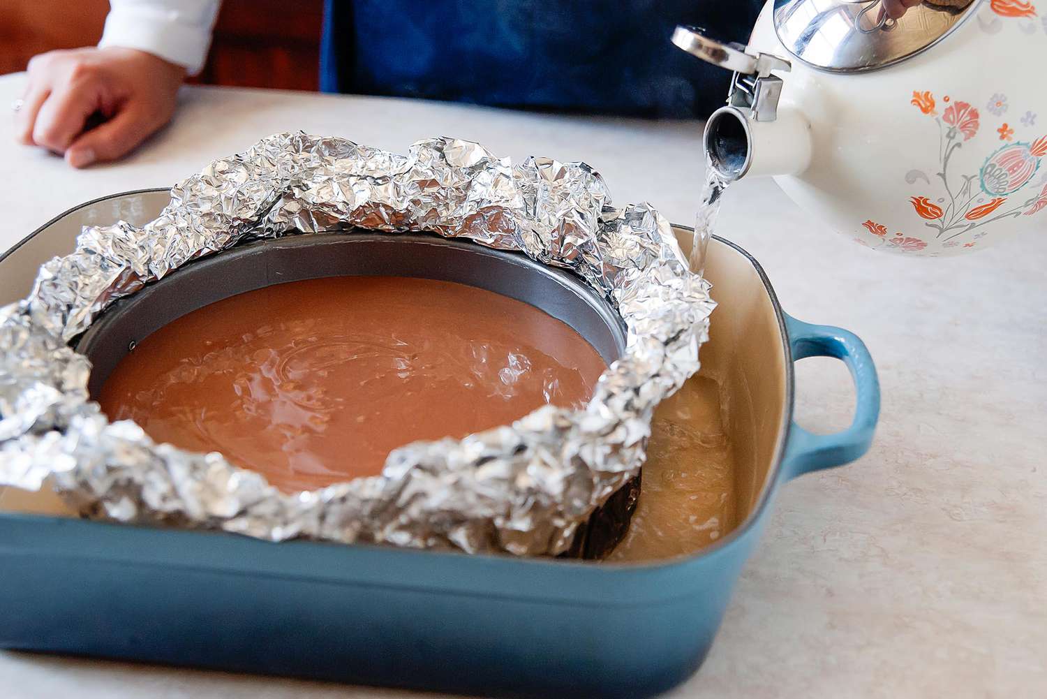 Chocolate cheesecake in waterbath. Person holding tea kettle with water to illustrate how to save a cheesecake if it gets wet.
