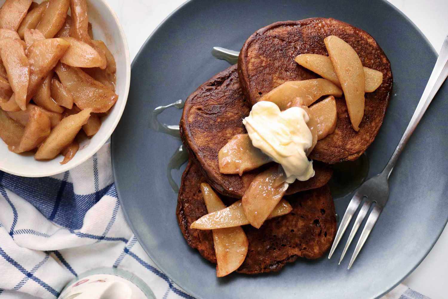Christmas morning pancakes spread on a plate and topped with pears and creme fraiche. Additional pears are in a bowl next to the plate.