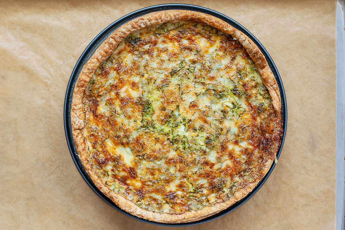 An Easter quiche baked in a springform pan and cooling on baking sheet covered in parchment paper.