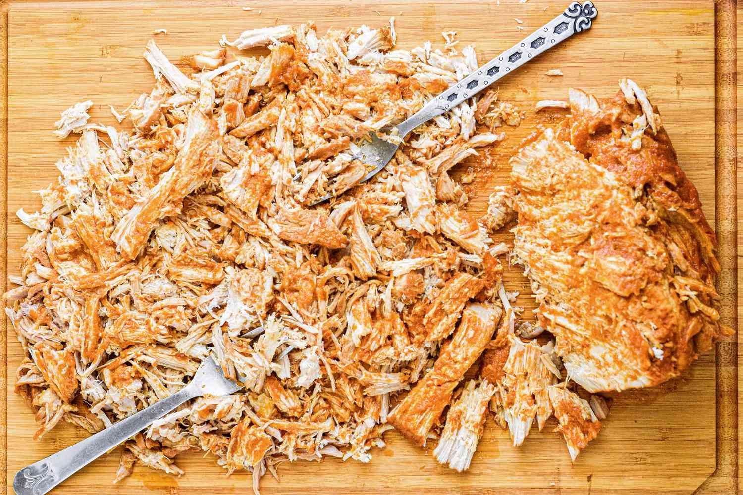 Pulled pork shredded on a cutting board with two forks.