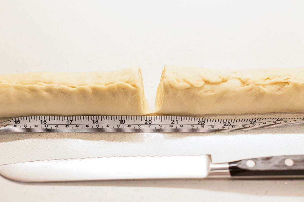 Side view of lion house dinner roll dough cut down the middle with a measuring tape in front of it.