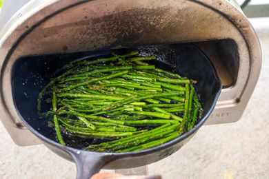 Roccbox pizza oven with a cast iron skillet of asparagus being pulled out of it.