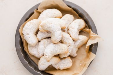 Overhead view of crescent cookies on parchment paper in a pan.