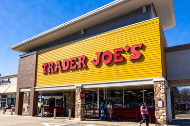 Photo of the front of a Trader Joes' store showing the main entrance with the red logo on a yellow background