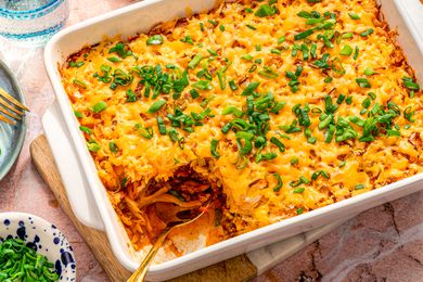 shipwreck casserole in a casserole dish at a table setting with a bowl of scallions, plate, and glass of water 