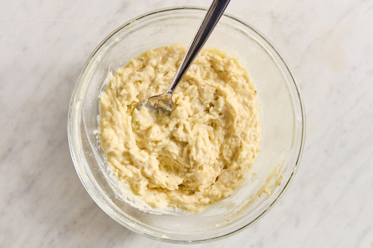 Overhead view of a clear glass bowl of potato batter with a fork from Boxty (Irish Potato Pancakes) recipe