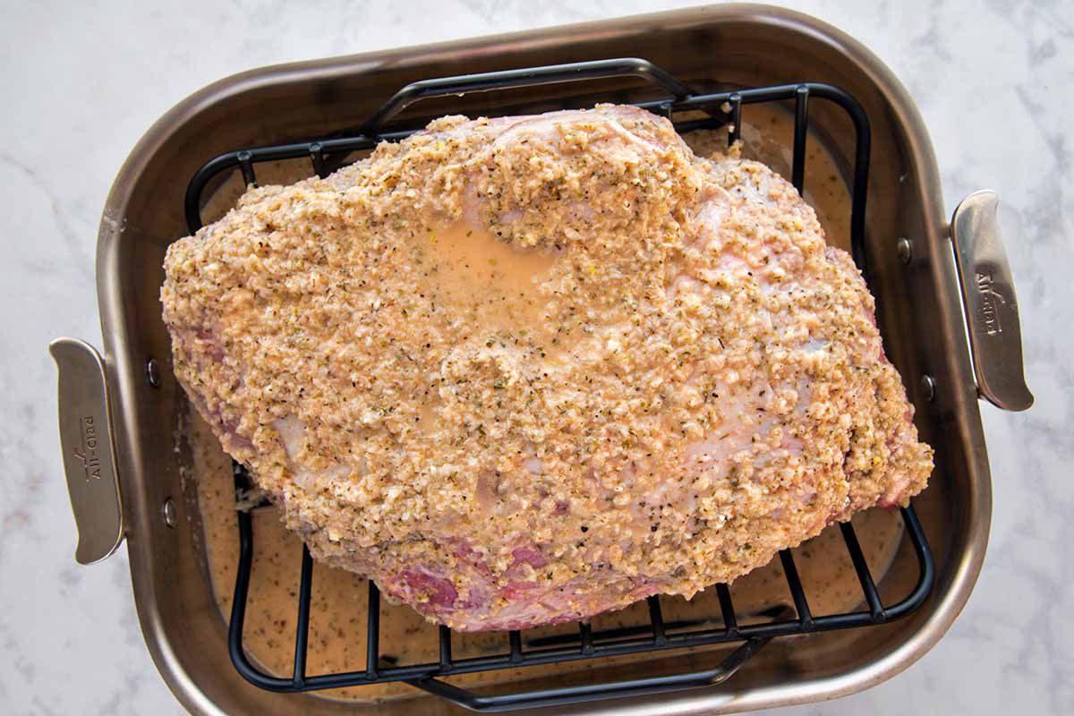 Cuban-style pork roast covered in golden marinade and resting on a rack in a roasting pan. The pan rests on a marble background.