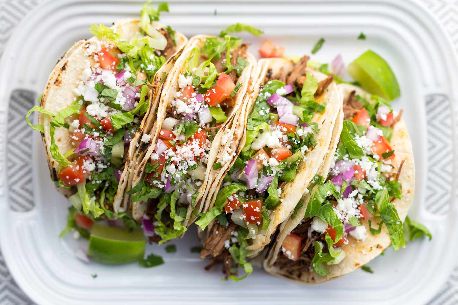 Four tacos topped with lettuce, cheese, tomatoes, and red onion