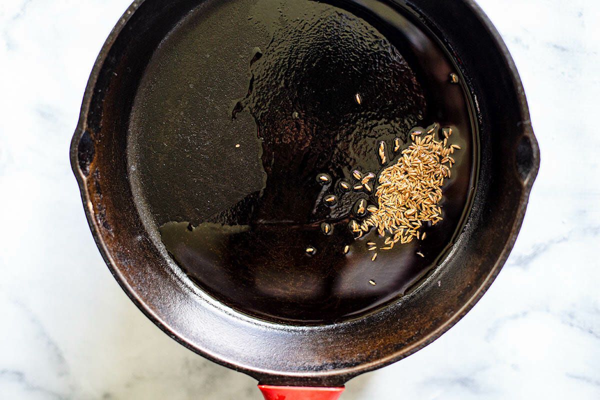 Cumin seeds being toasted in a black skillet for vegetable samosa filling.