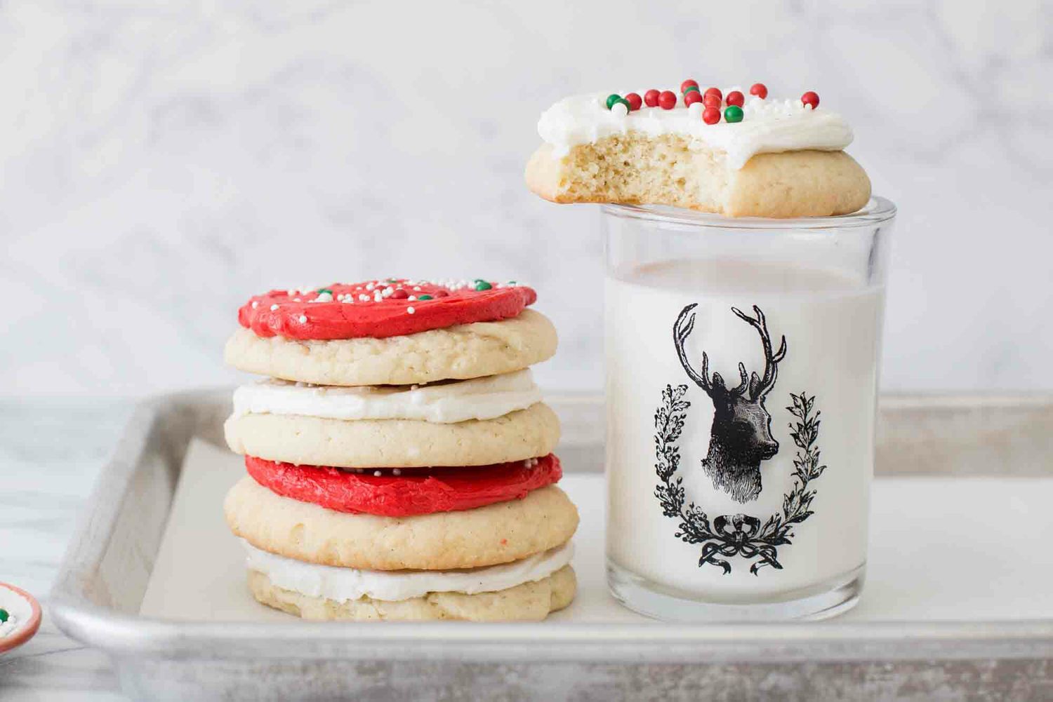 A small stack of red and white frosted cookies set next to a glass of milk.