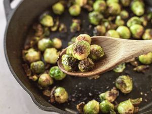 A wooden spoon scooping up roasted brussel sprouts in a cast iron pan.