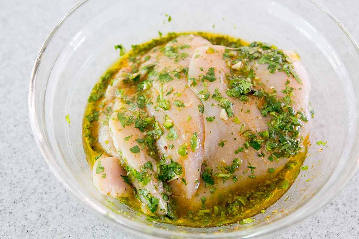 Chicken being marinated in a glass bowl 