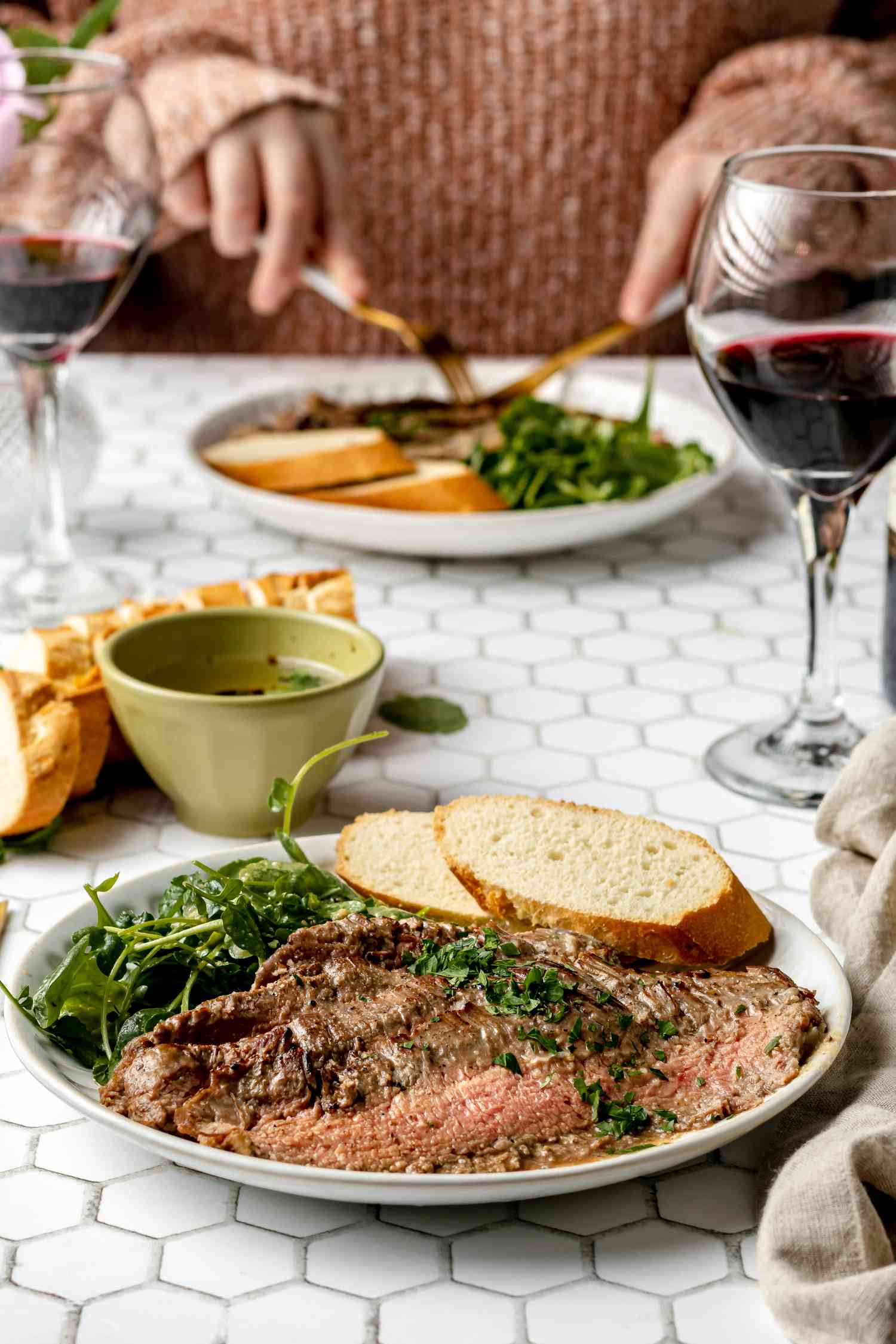 Side view of a person eating flank steak and a plate of flank steak in front of the person.