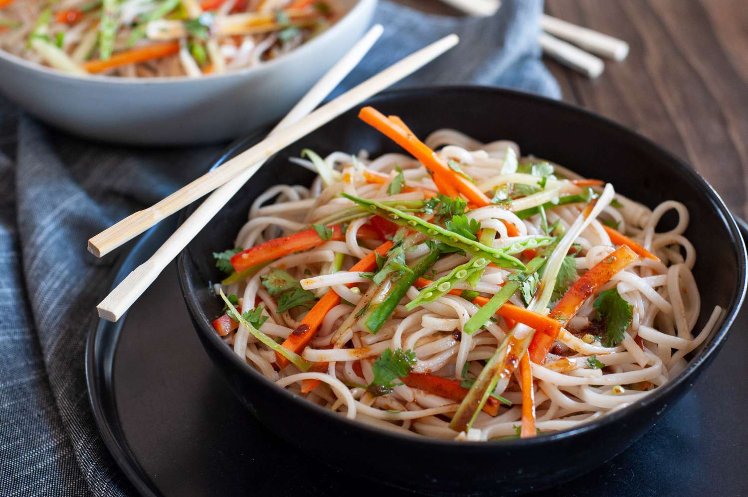 Rice noodle salad with sesame dressing in a black bowl and topped with thinly sliced vegetables.