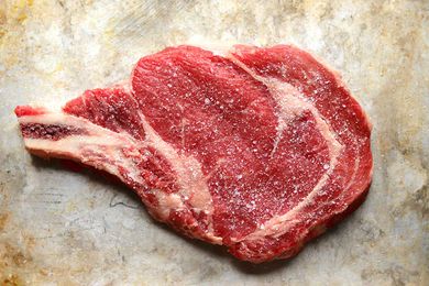 A bone-in raw steak seasoned with salt and set on a worn baking sheet.