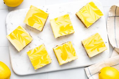 Lemon Cheesecake Bars on a Marble Board, and on the Counter, Lemons and a Kitchen Towel