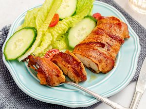 Bacon-Wrapped Chicken on a plate with a small side salad and a knife and fork