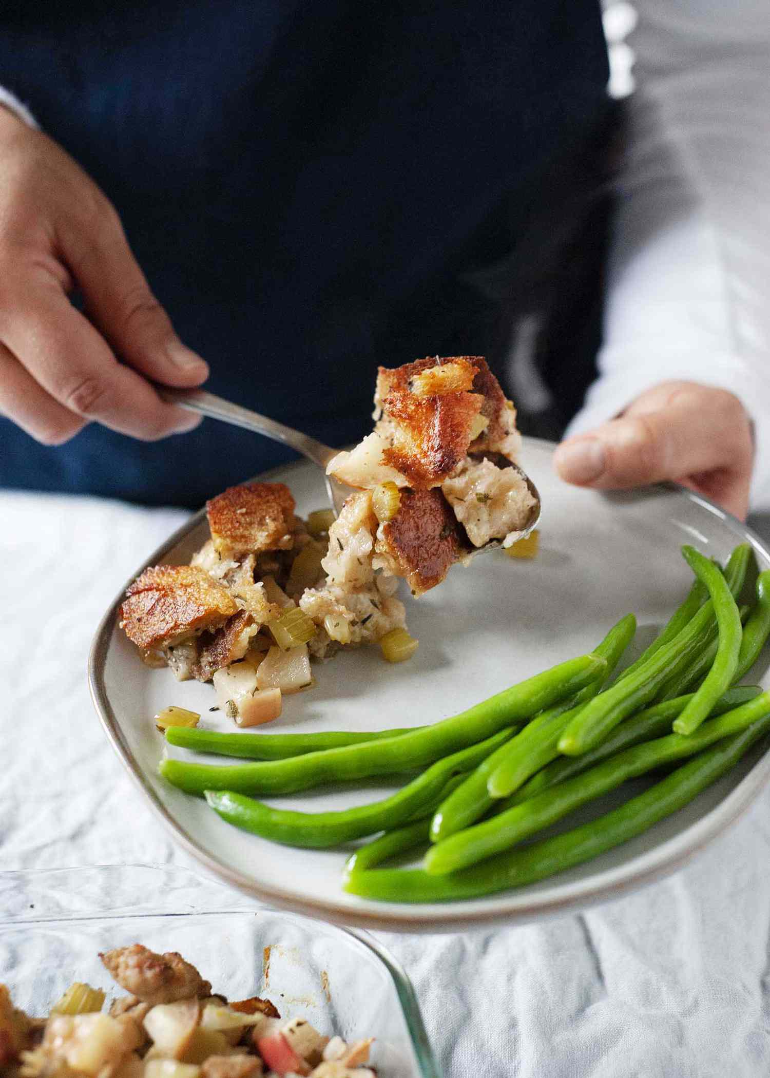 Woman putting classic sauage stuffing onto a plate with green beans.
