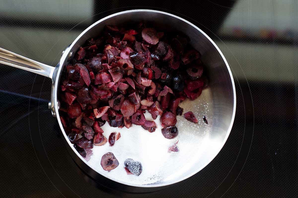 Sugar added to cherries in a saucepan for Homemade Black Forest Cake.
