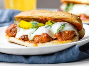 A Plate of Meatball Sub Topped with Banana Peppers and Basil, and in the Background, a Plate With Another Sub and a Glass of Beer