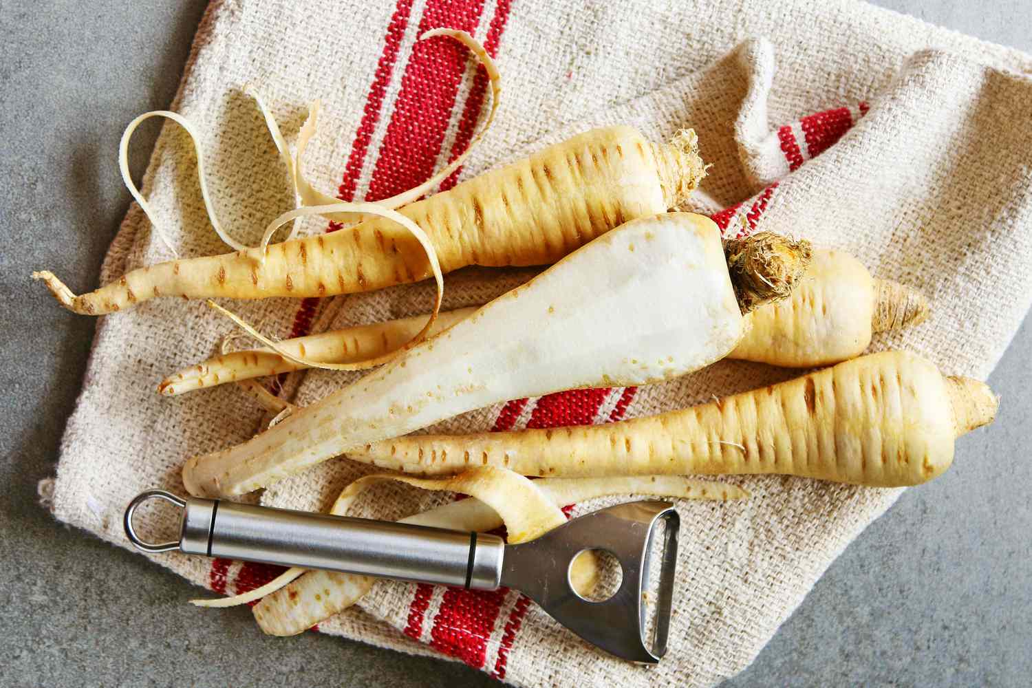 Parnsips on a kitchen towel in the process of being peeled with a vegetable peeler