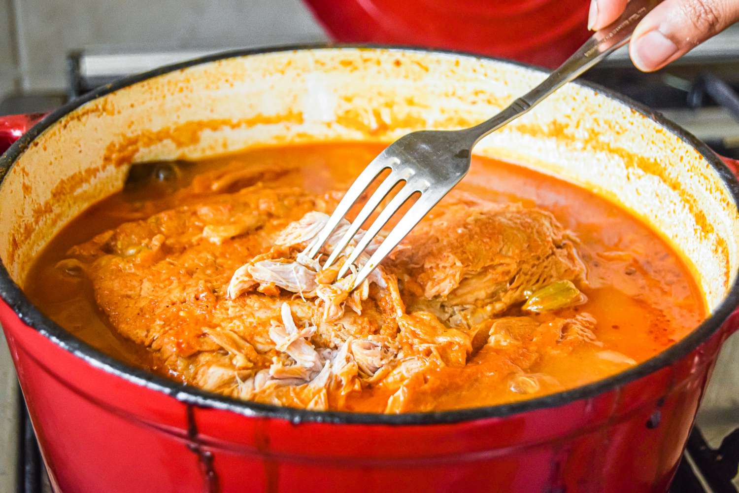 A dutch oven with a fork shredding the pork to show how to make pulled pork.