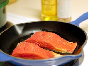 Two salmon fillets cooking in a blue skillet