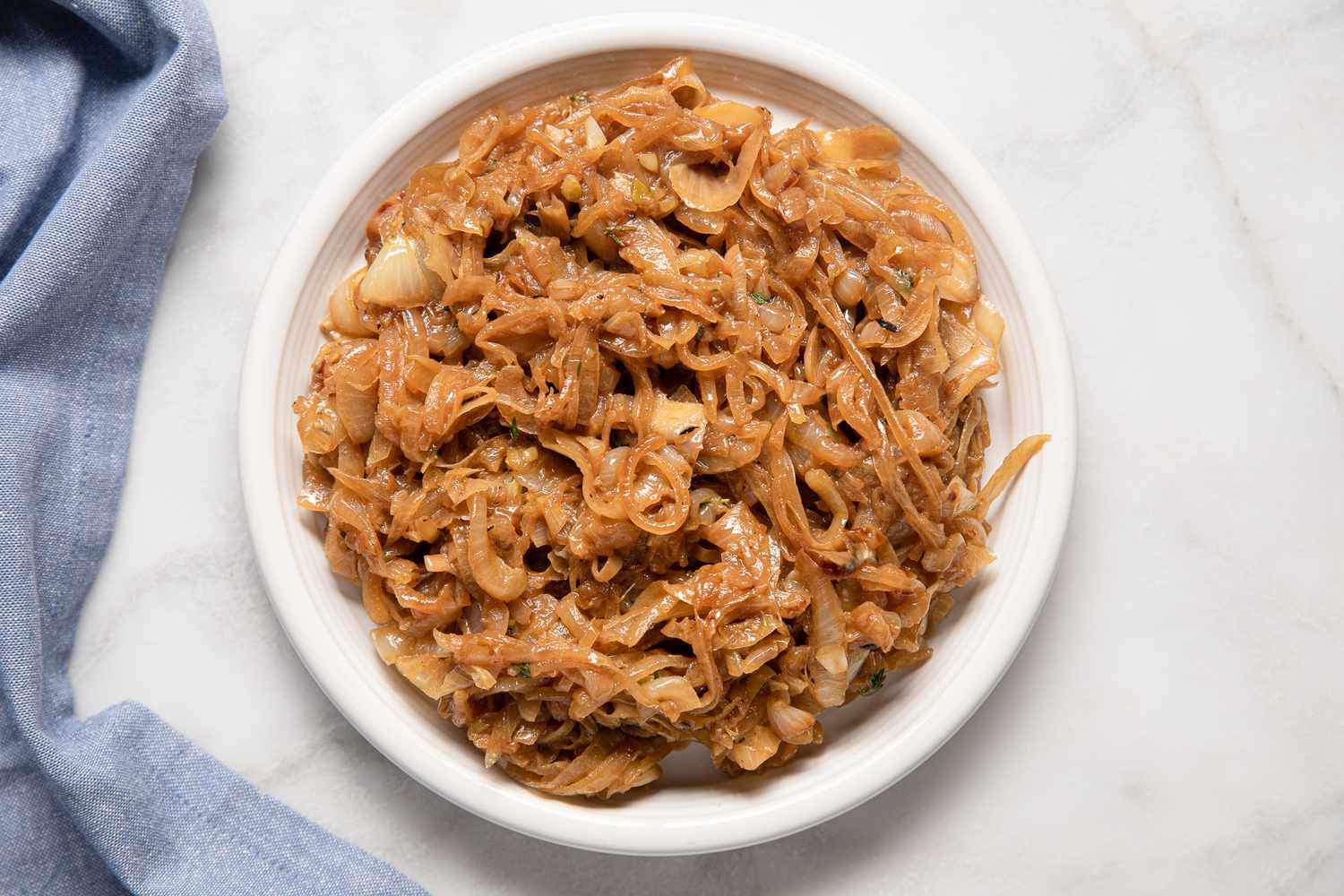 Bowl of Caramelized Onions Next to a Light Blue Kitchen Towel for French Onion Meatballs Recipe