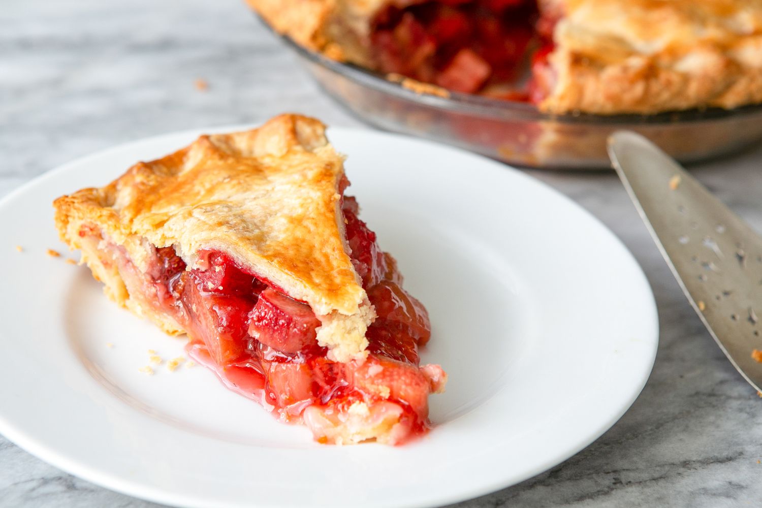 Slice of Strawberry Rhubarb Pie on a Plate, and in the Surroundings, More Pie in a Glass Pie Pan and a Pie Server