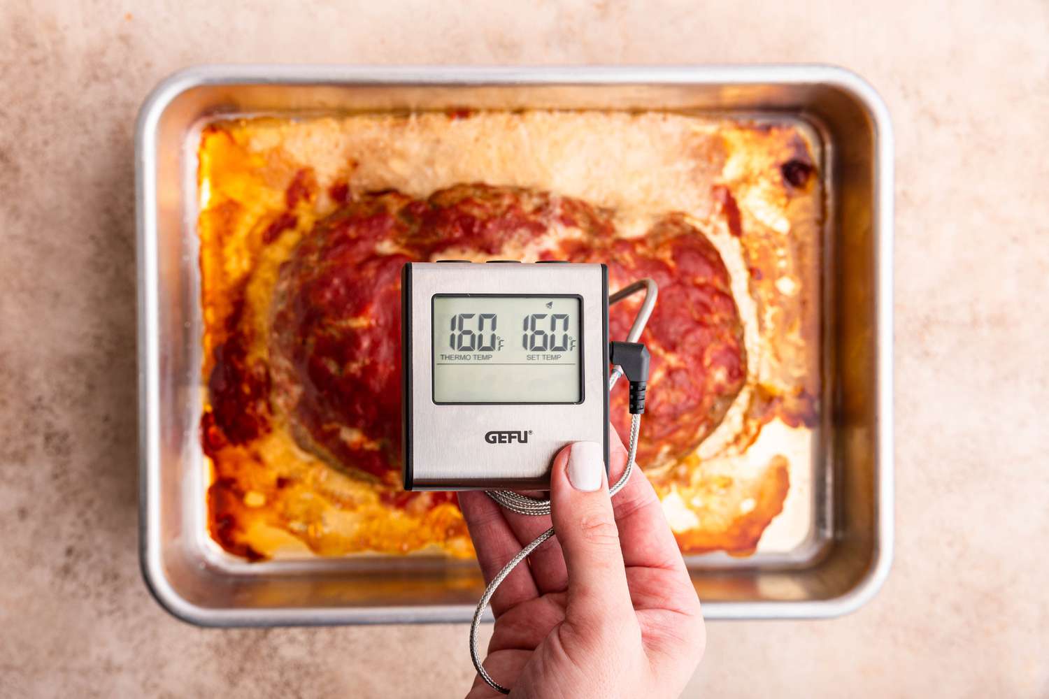 Digital Thermometer Showcasing 160F, and Underneath It, the Cooked Meatloaf on the Baking Pan