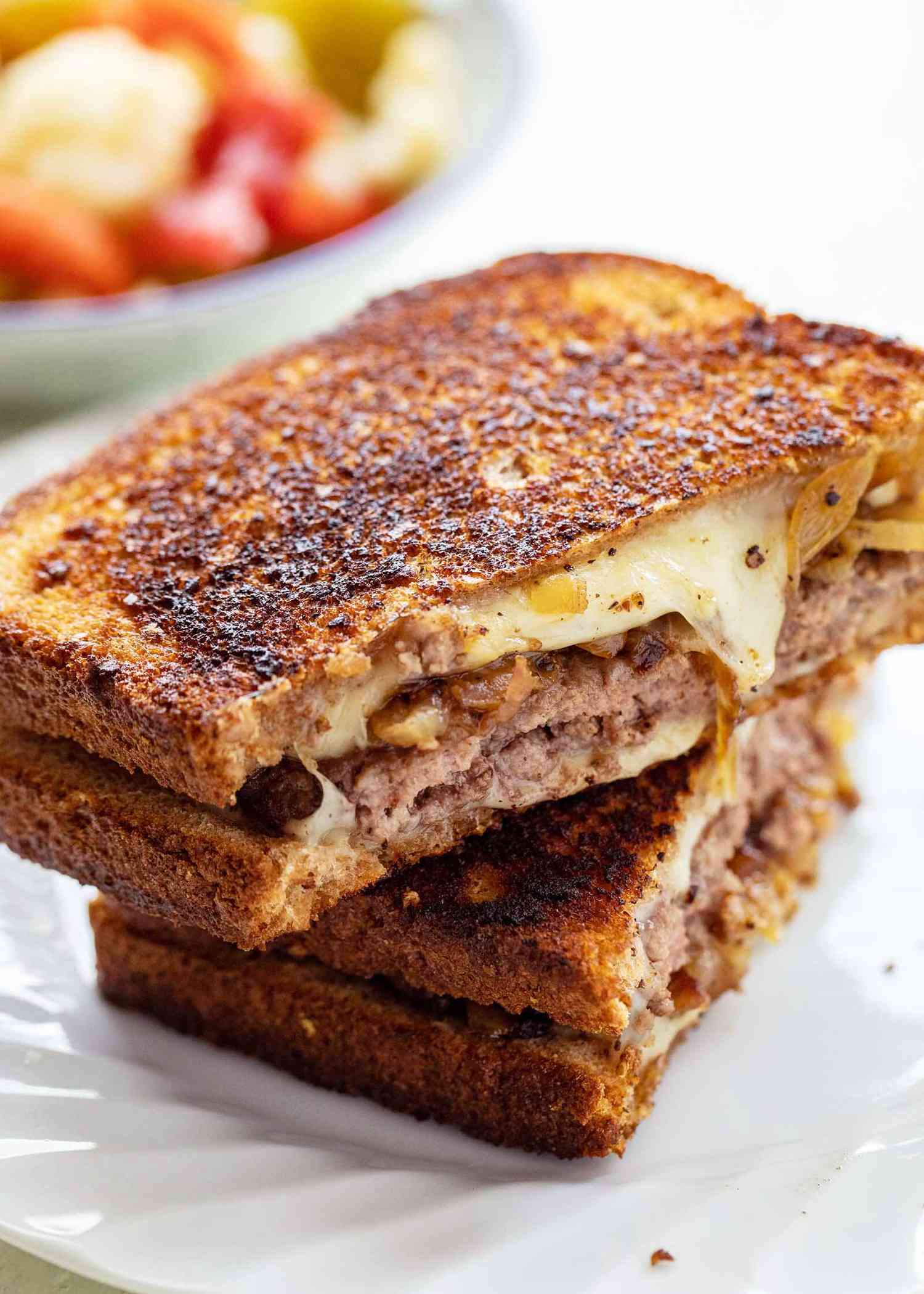 The best patty melt sliced in half and stacked on top of each other. The sandwich is crispy with melted cheese, caramelized onions and beef patties visible.