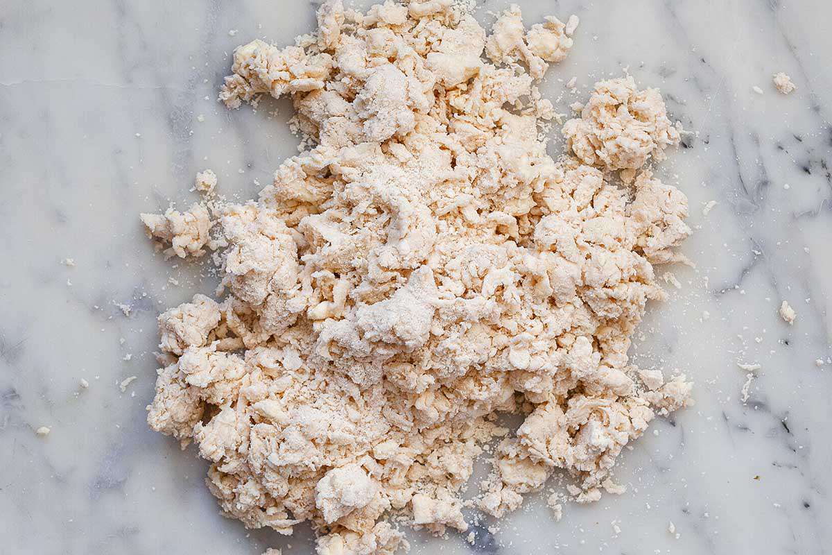 A shaggy dough for homemade deep-dish quiche is on a marble countertop.