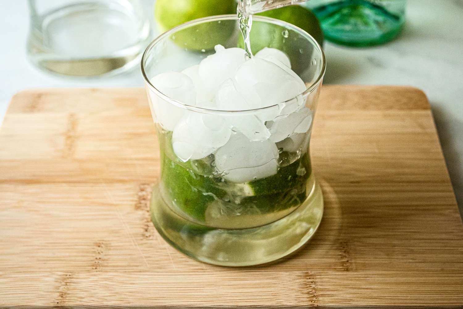 Adding ice and cachaça to a rocks glass to make a Brazilian caipirinha.