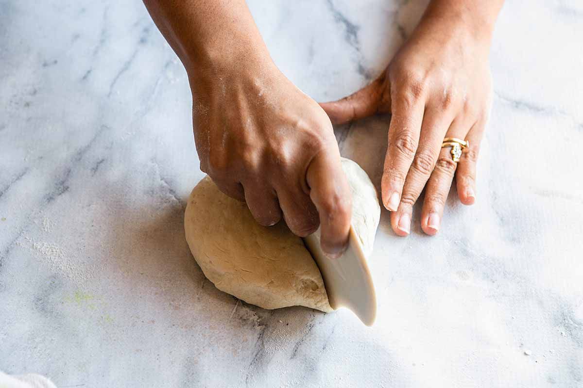 Homemade Naan Recipe - person cutting ball of dough into smaller pieces