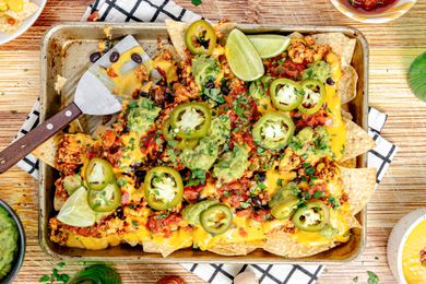 Baking Sheet of Vegan Nachos (Nachos Topped with Salsa, Queso, Pickled Jalpenos, and Two Lime Wedges) with a Serving Missing 