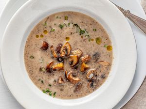 Chestnut mushroom soup in a white bowl with a white plate underneath.