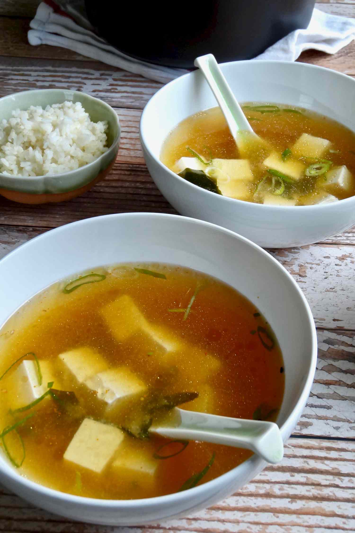 Two bowls of quick and easy miso soup with spoons and a small side of rice.