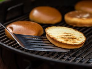 Spatula with a toasted hamburger bun on a grill.