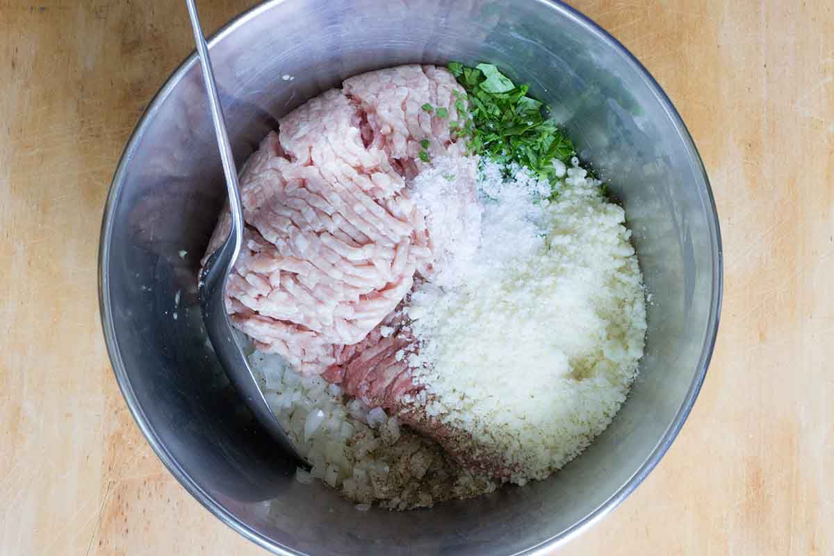 Italian wedding soup ingredients in a metal bowl.