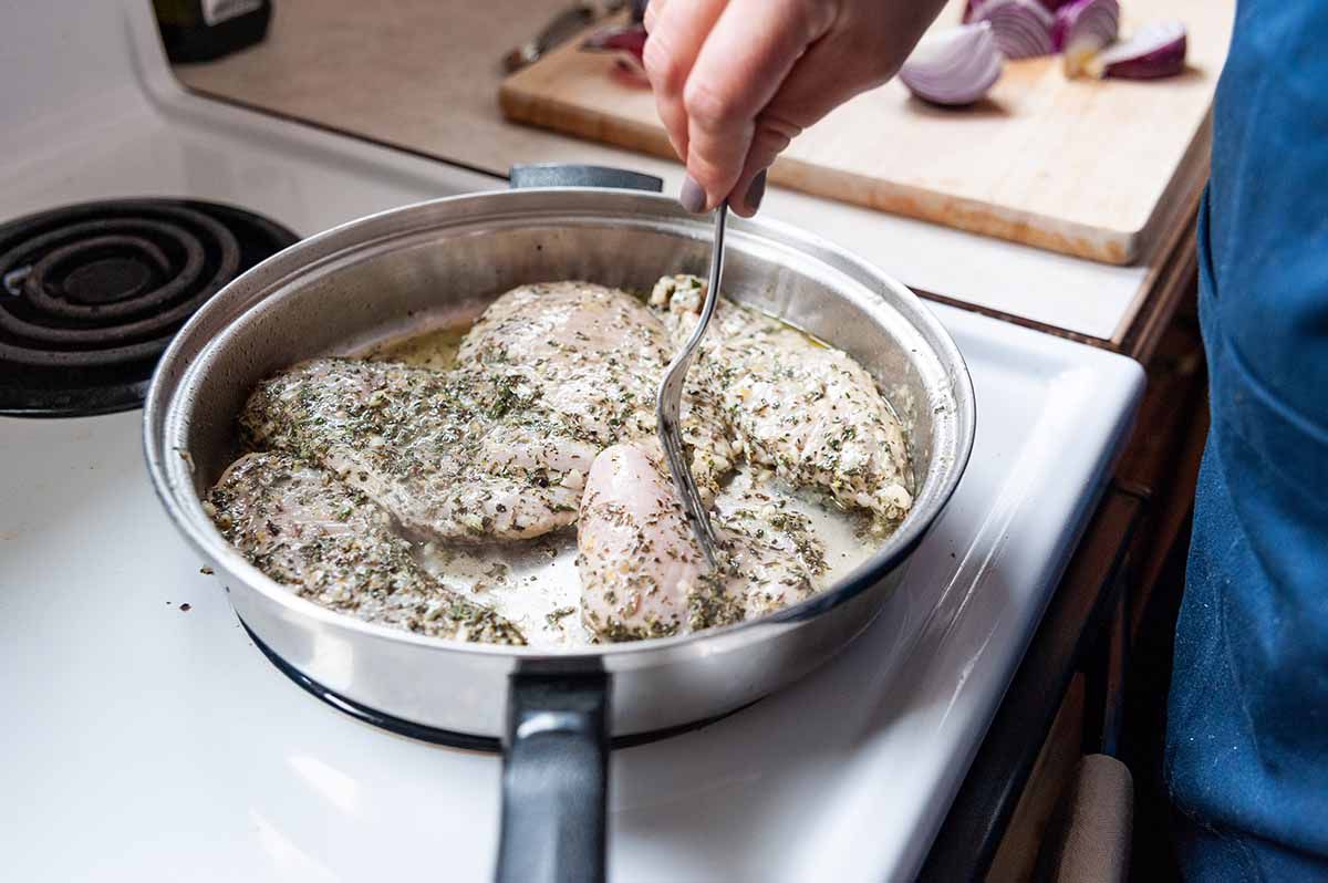 Chicken Freezer Meal with Chicken Tenders-woman's hand holding a fork and moving a chicken breast around inside a silver skillet breast