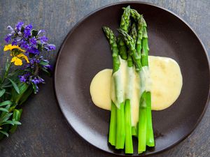 Steamed asparagus on a dark plate topped with Hollandaise sauce