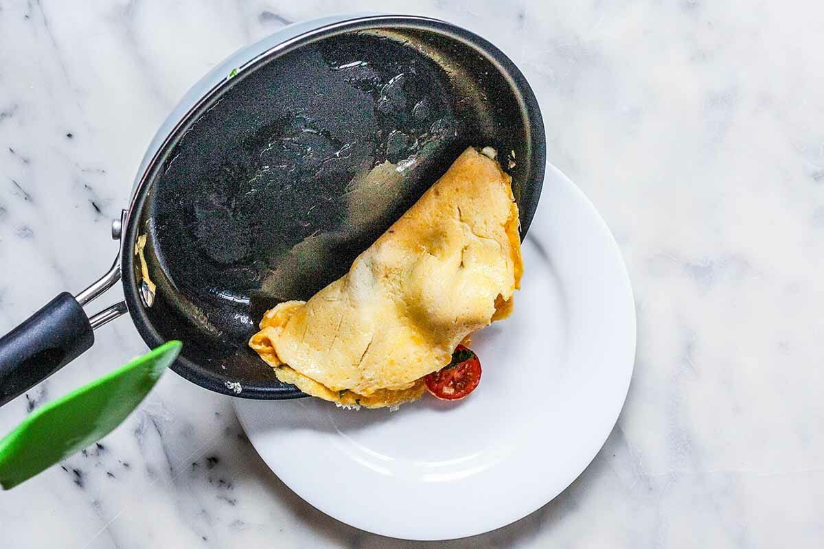 Cooked omelette being slid out of the non-stick pan and onto a white plate